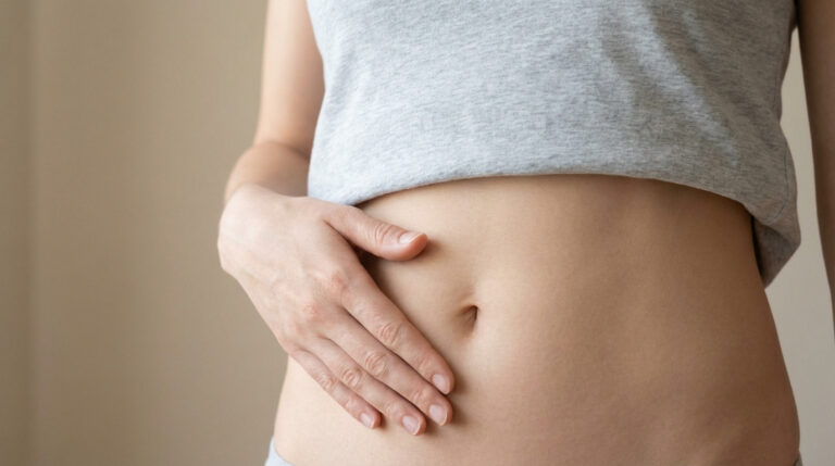 Close-up of a person's midsection, a hand gently touches the smooth skin around the navel. Light grey top, soft lighting, calm mood.