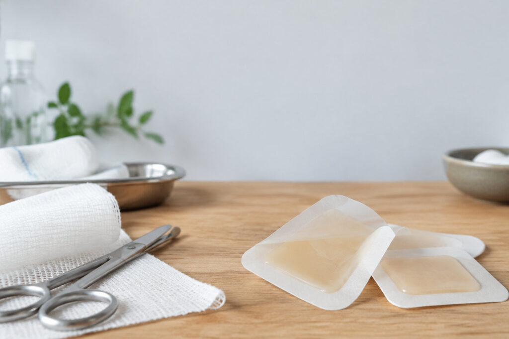 Pansements hydrogel posés sur une table en bois avec des ciseaux médicaux et des compresses en arrière-plan.